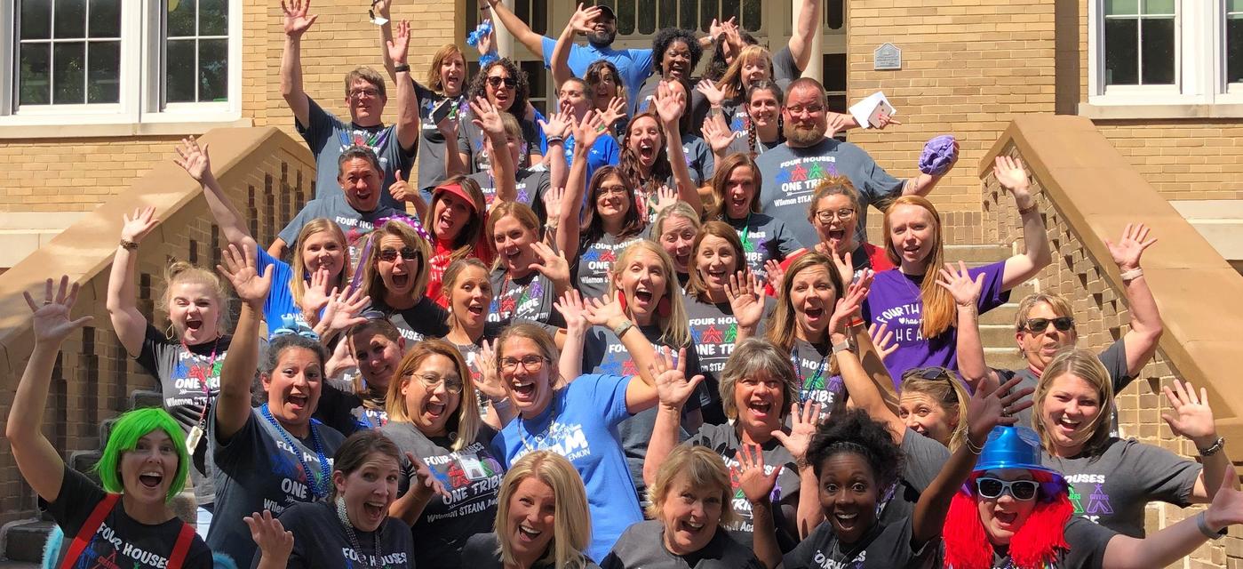 faculty and staff with hands raised on front steps