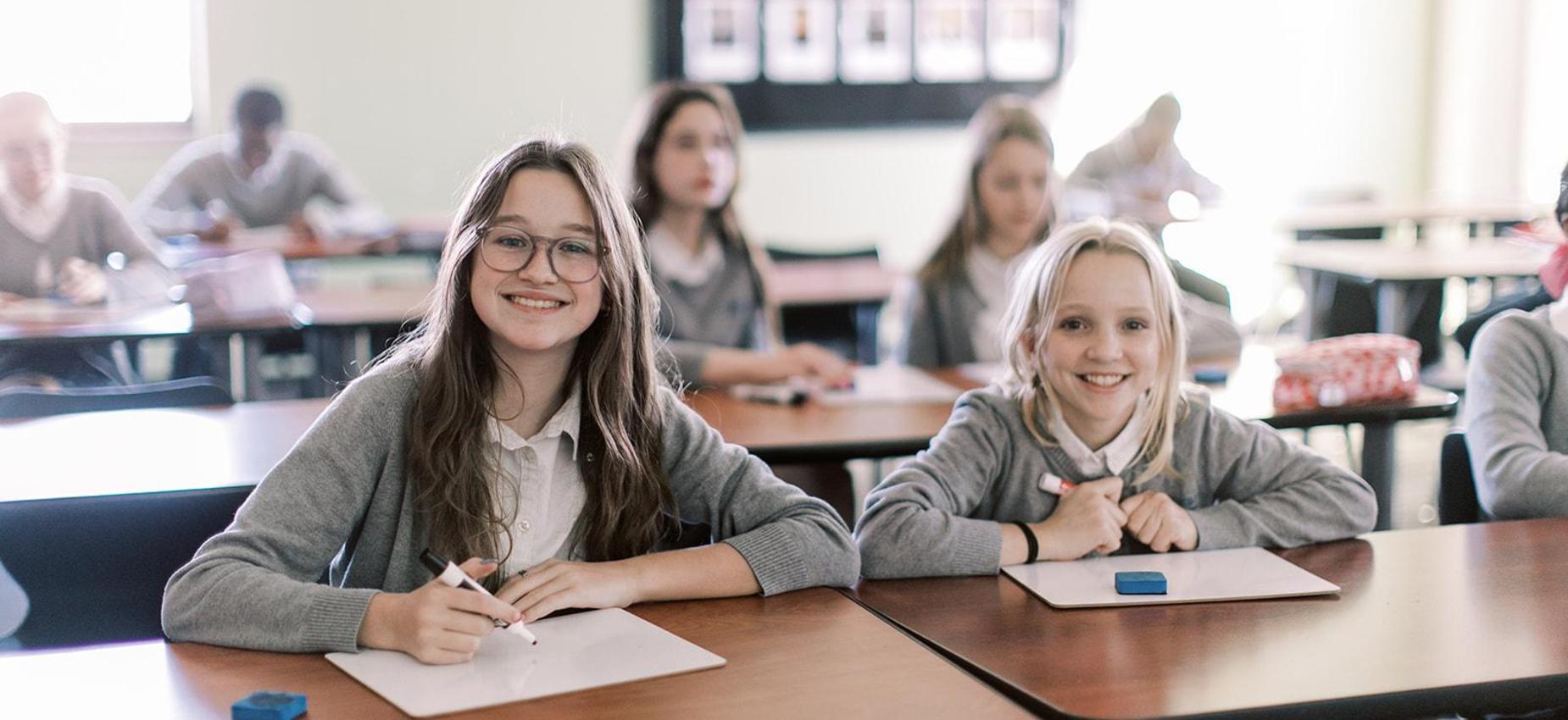 Two smiling students at their desks during class at Founders Classical Academy &ndash; Frisco
