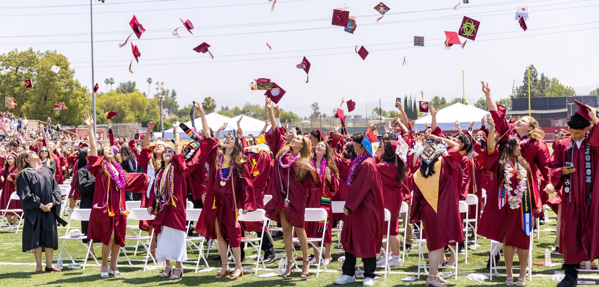 Graduates toss their caps into the air during a jubilant outdoor ceremony.