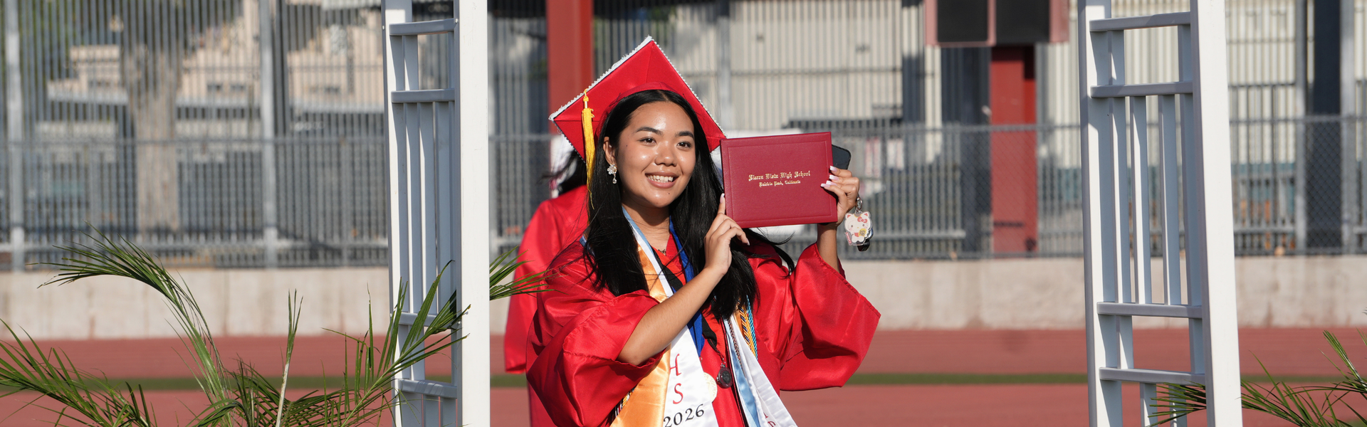 Graduate in a red gown holding a diploma, smiling at the camera.