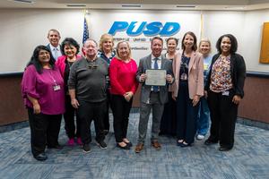 Jonathon Dodson holds his Administrator of the Year certificate surrounded by colleagues at the PUSD Board meeting.