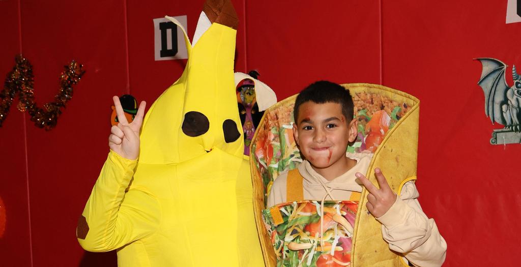 One boy dressed as a banana and one boy dressed as a taco, giving the peace sign.