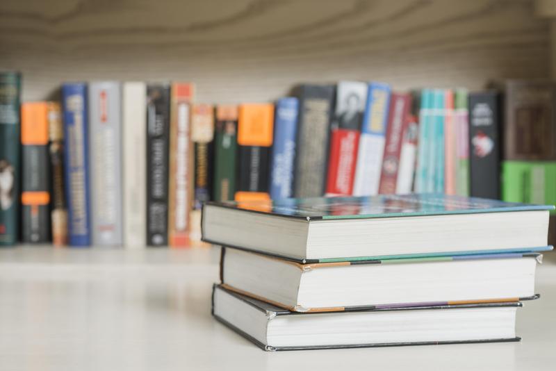 Three books near a bookshelf containing books