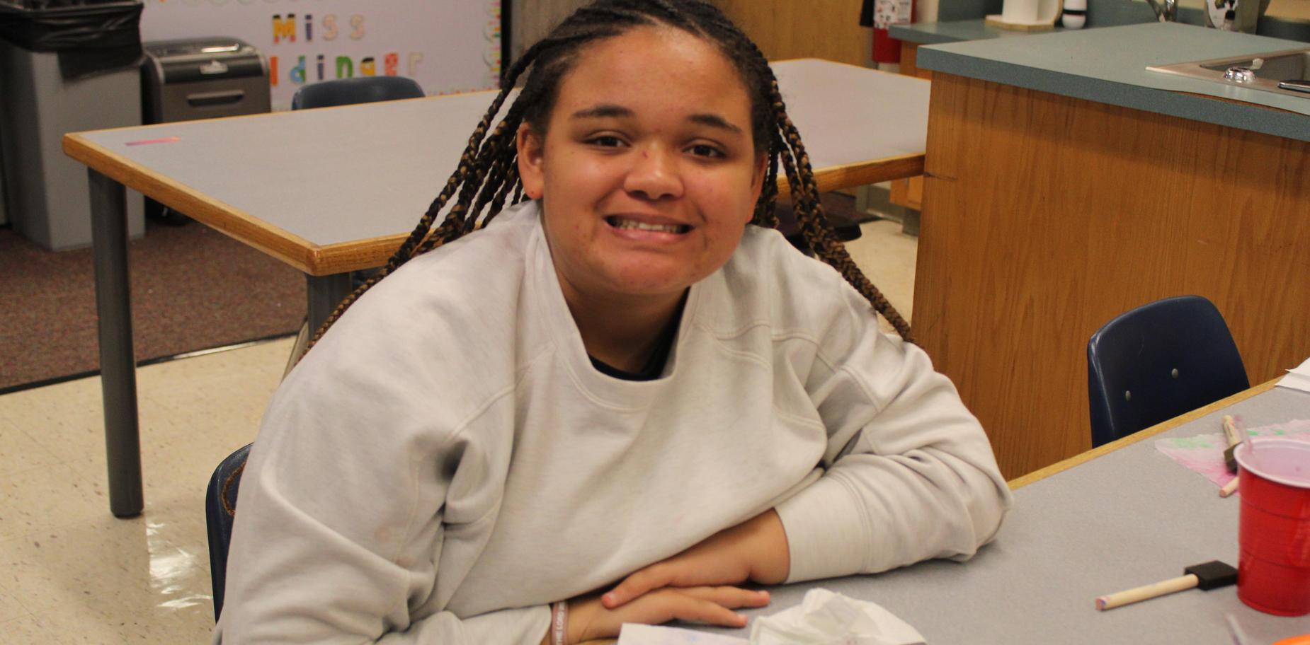 A girl smiles at the camera while working on an art project.