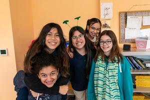 5 Students at Arco Iris Spanish Immersion School smile for a photo together in a classroom.