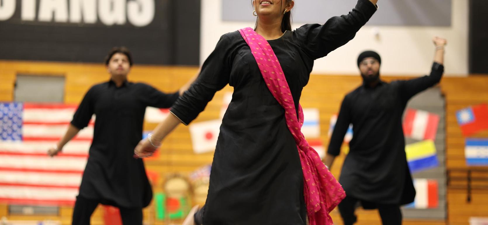 A performer in traditional attire dances energetically, flanked by two male dancers.