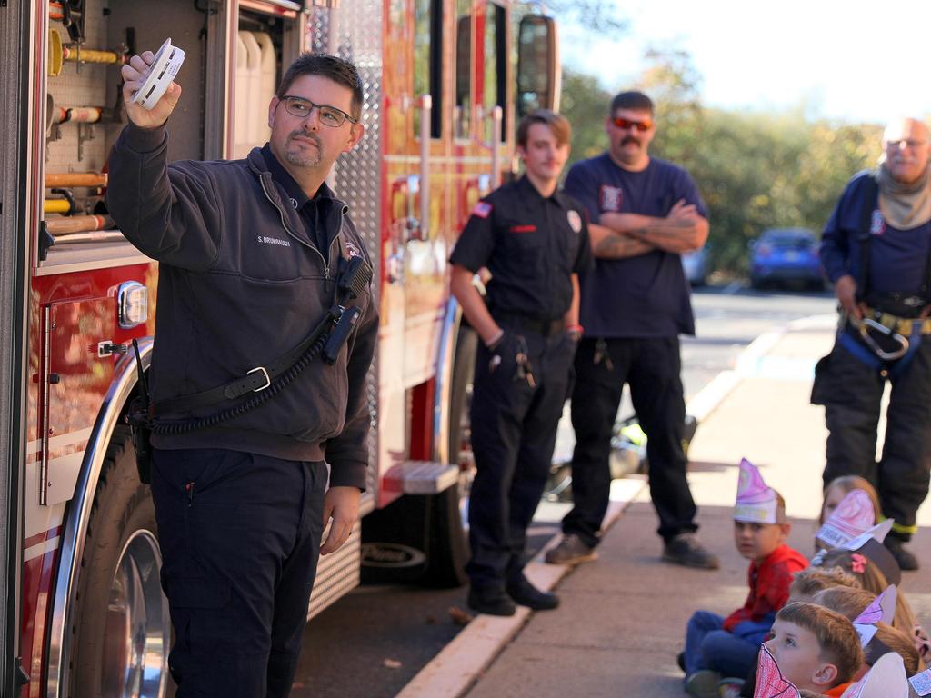 Firefighters standing in front of a firetruck teaching students about smoke detectors.
