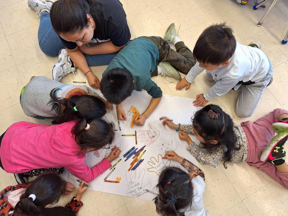 Group of children coloring and drawing together on a large sheet.