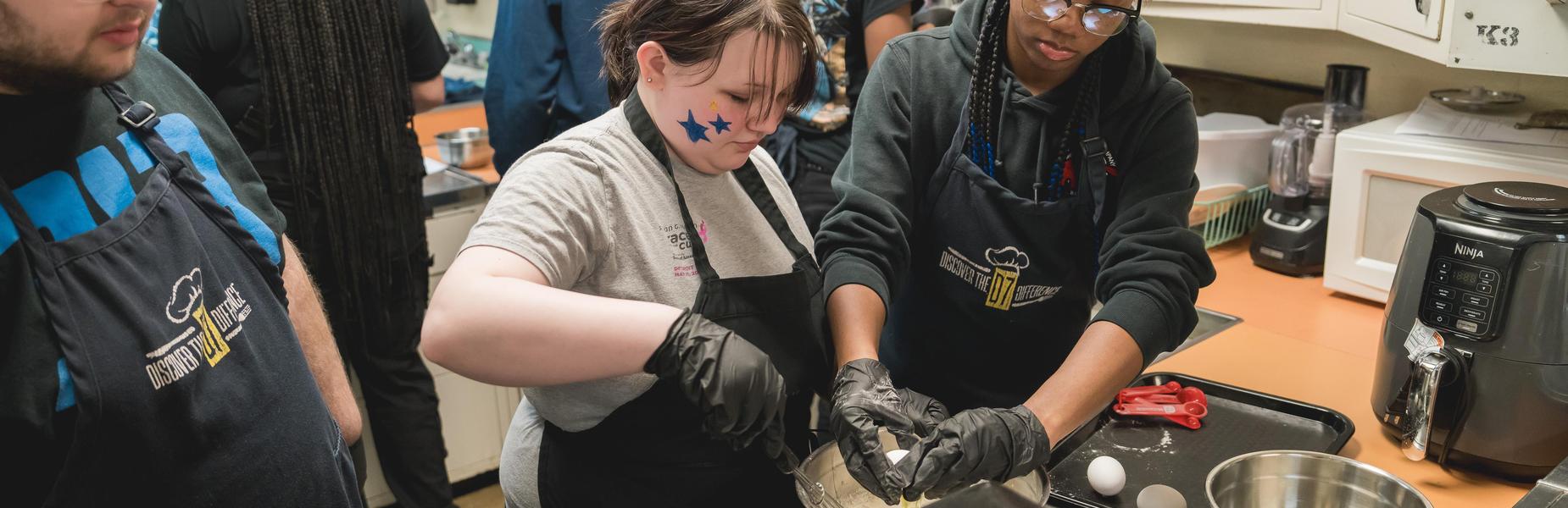 Two students mixing ingredients together while one has a star painted on their face.