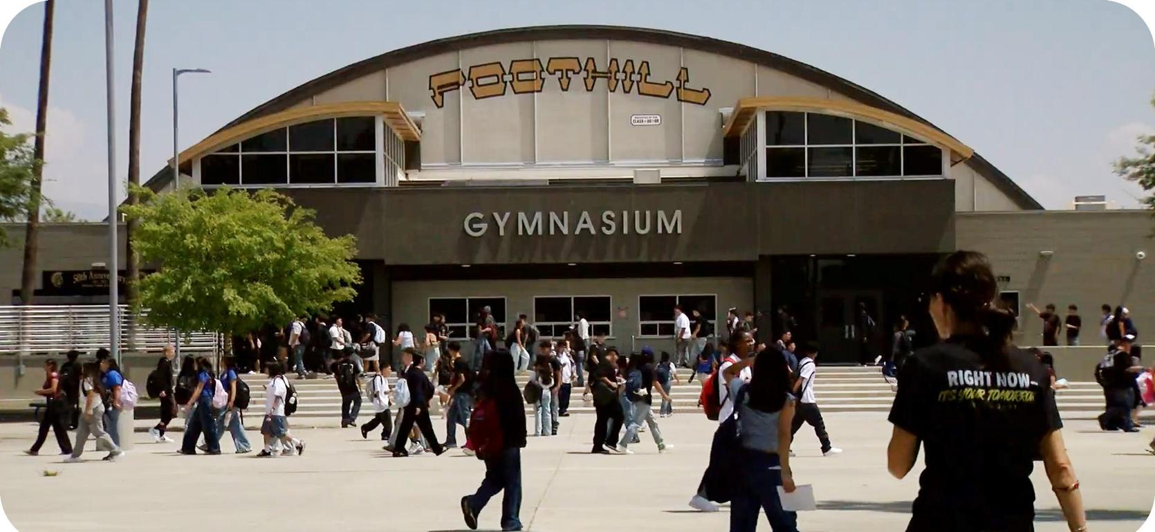Busy school exterior with students walking in front of a gymnasium.