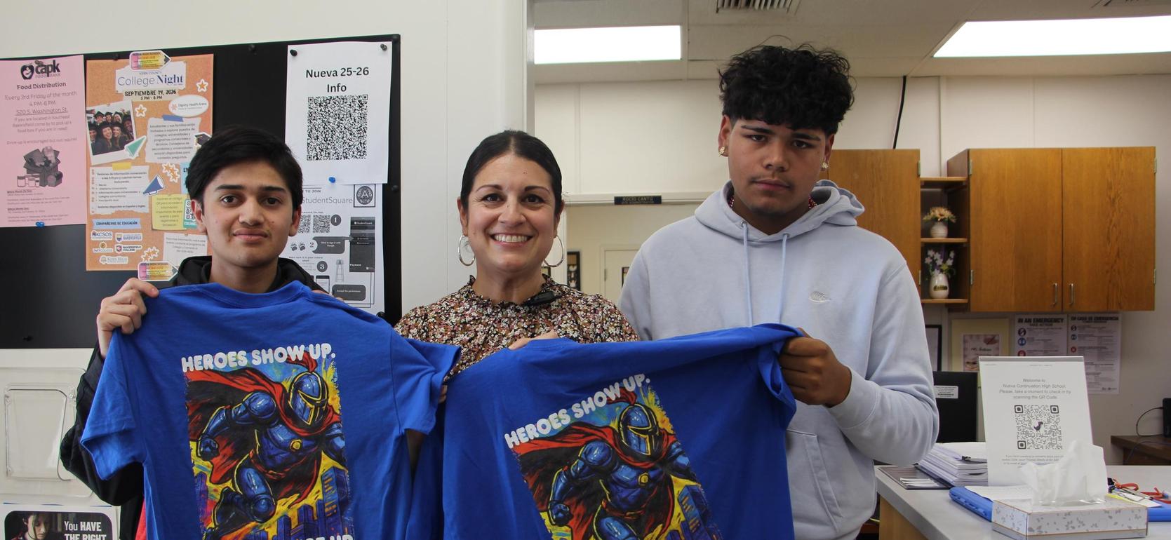 Three people hold up blue t-shirts featuring a heroic character and a motivational slogan.