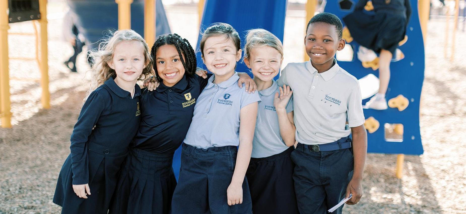 Five smiling elementary students in Founders uniforms on the playground