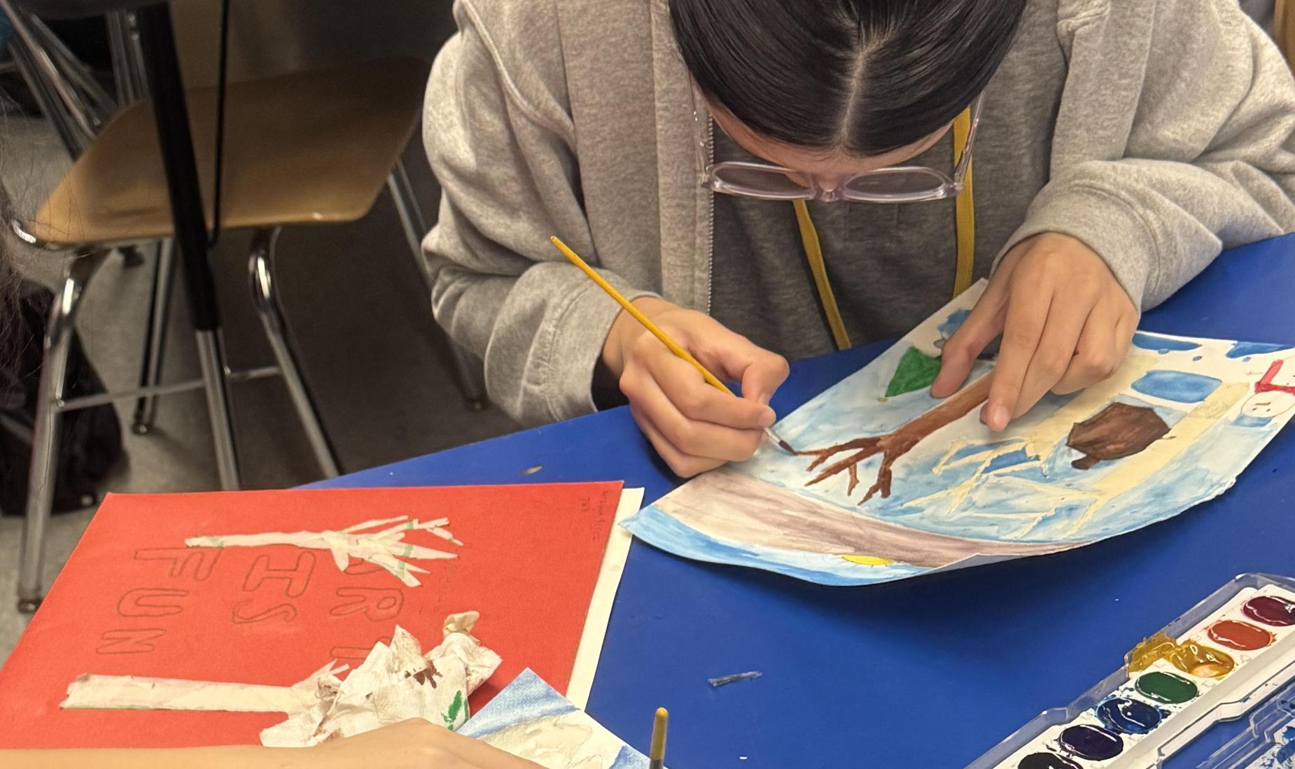 Two students using water colors for a nature scene.
