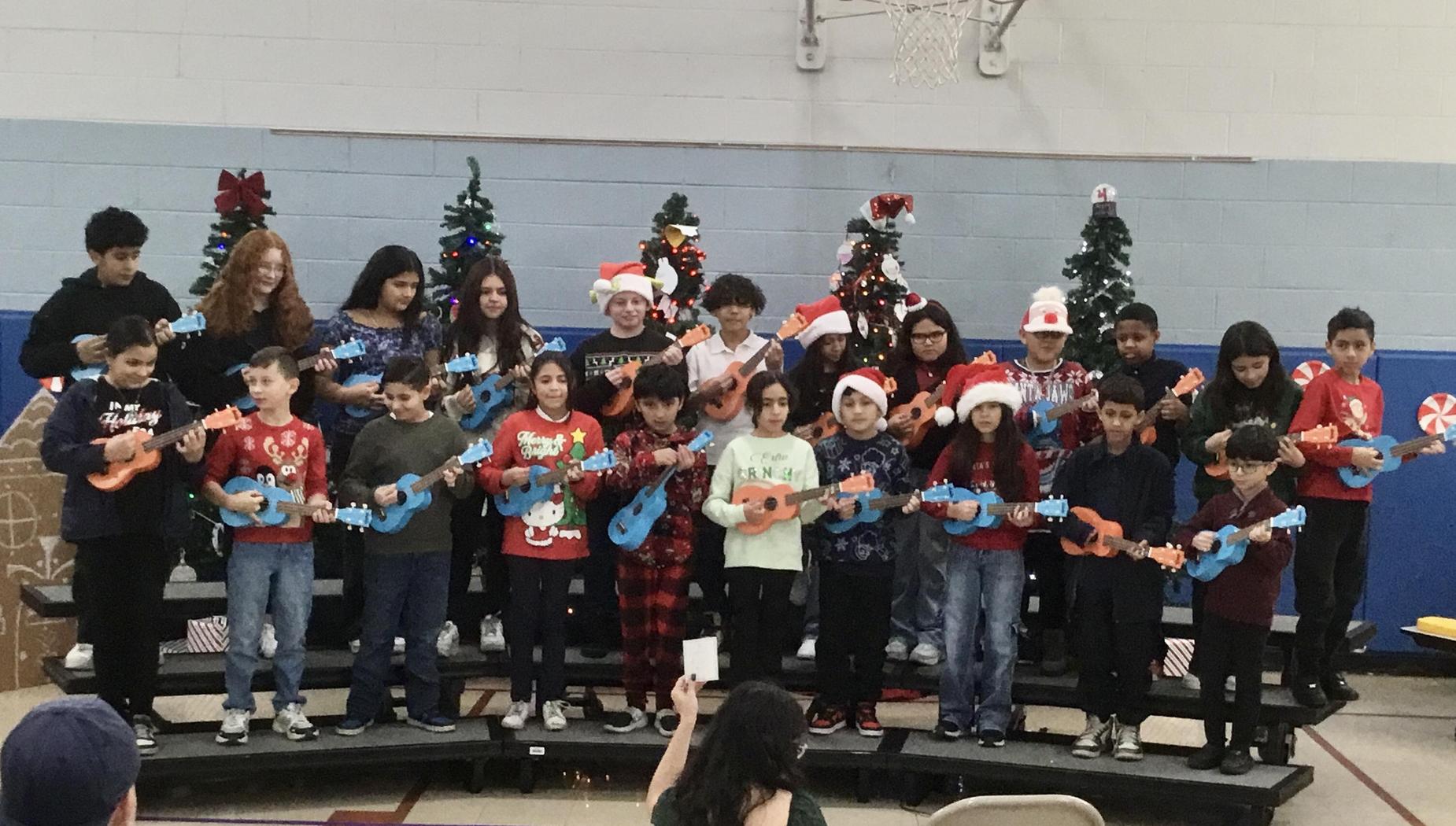A choir of children playing ukuleles on stage, decorated for the holidays.