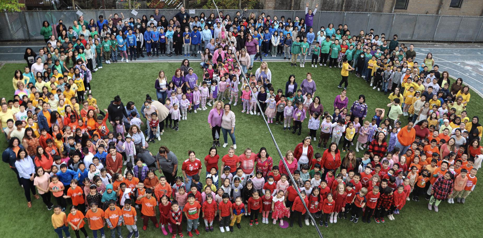 A large group photo of students and adults gathered on a field, wearing colorful outfits.