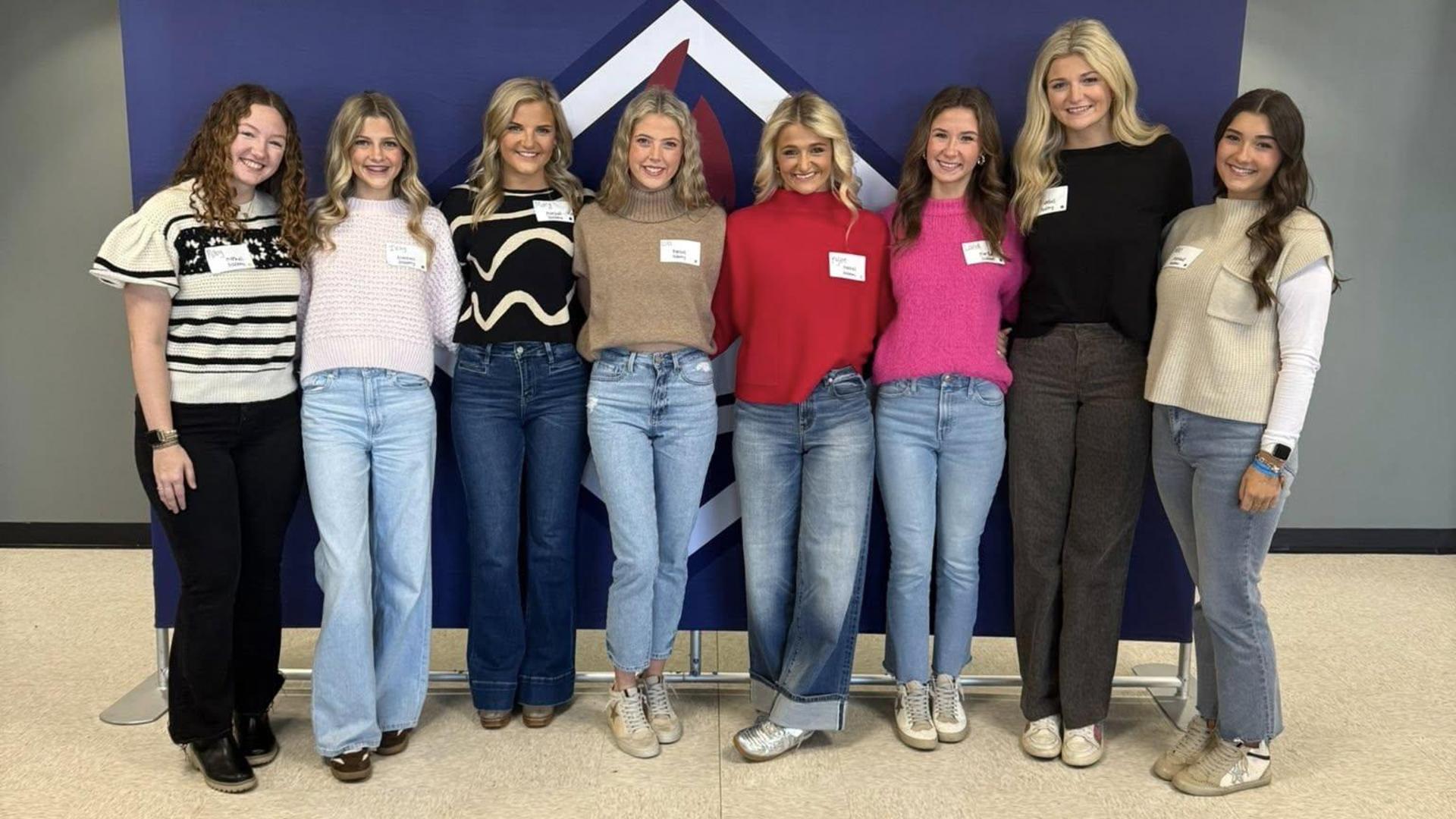 Group of women in casual attire stand together in front of a geometric backdrop.