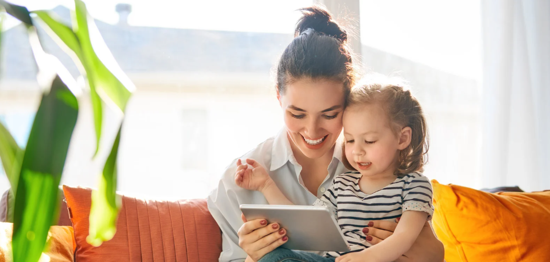 A woman and child happily reading on a tablet together in a bright room.
