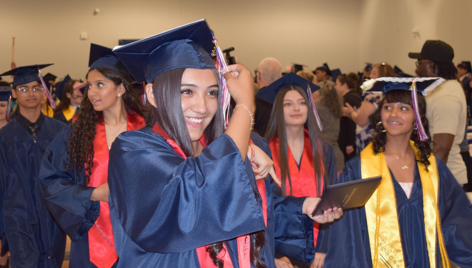 Graduates celebrate and adjust their caps in a crowded venue.