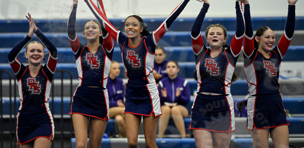 Cheerleaders perform a routine, raising their arms in excitement.