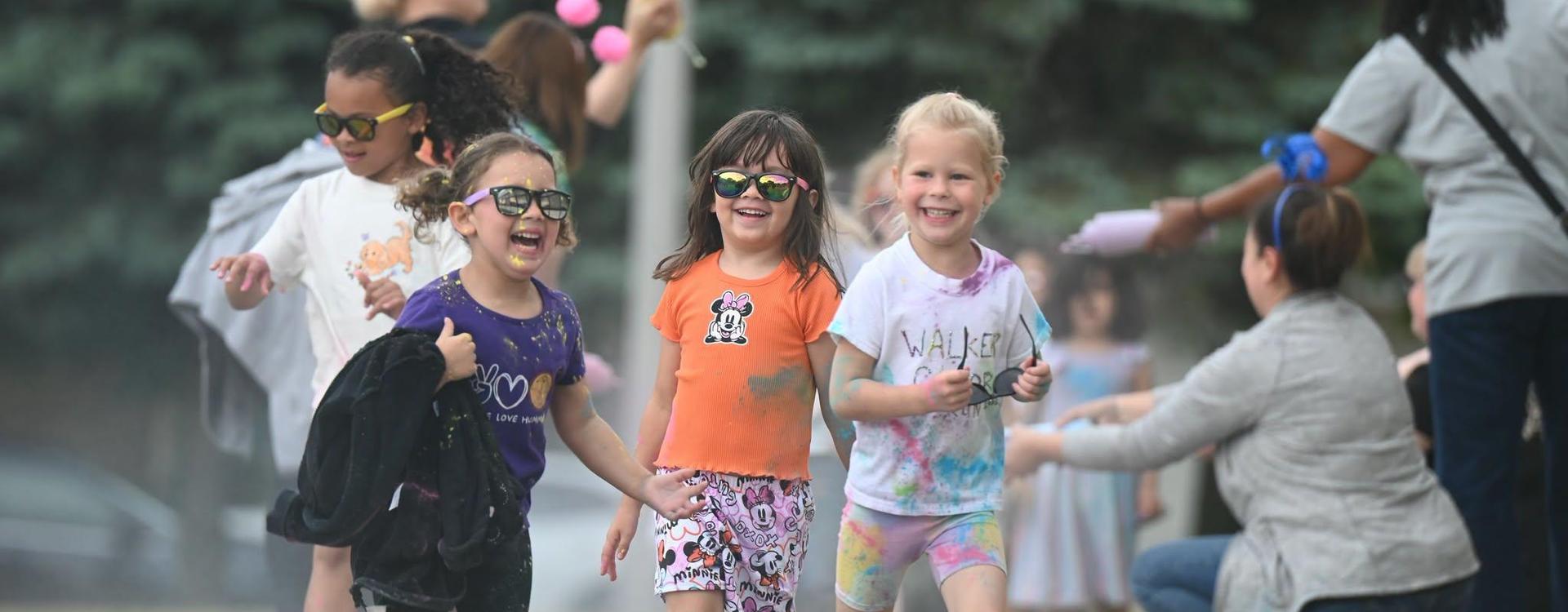 Children in sunglasses joyfully walking together at an outdoor event.