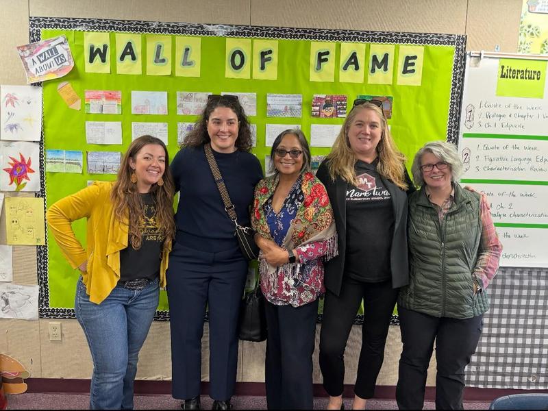 Five women stand together in front of a colorful Wall of Fame display.