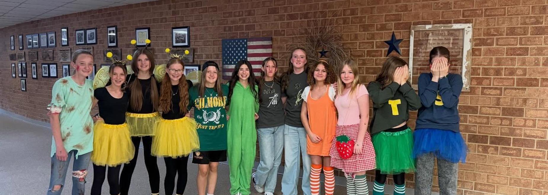 Group of girls in colorful tutus posing against a brick wall with decorations.