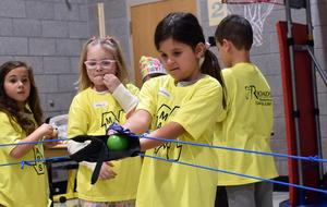 A girl in a yellow shirt pulls a green ball on a slingshot