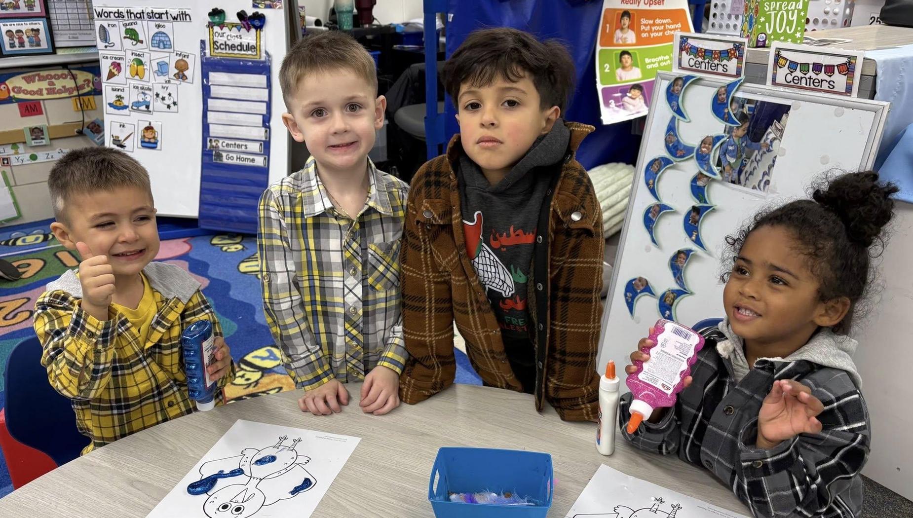 Four children at a table working on art projects in a classroom.
