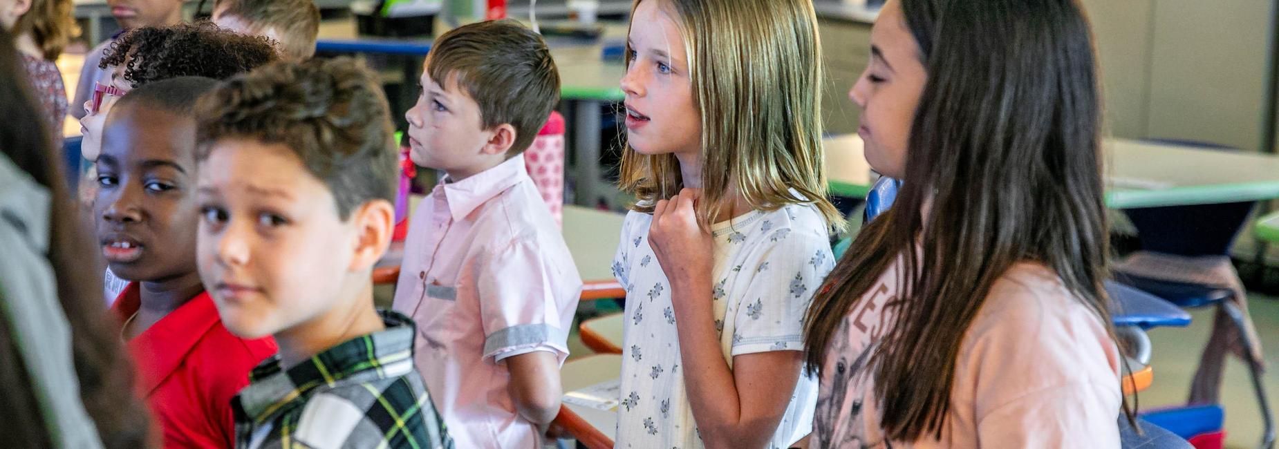A group of children standing in a line, participating in a classroom activity.