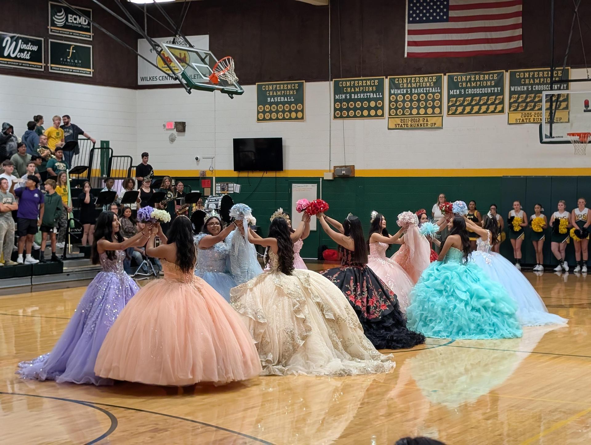 A group of girls in colorful ball gowns dancing together and showcasing their attire.
