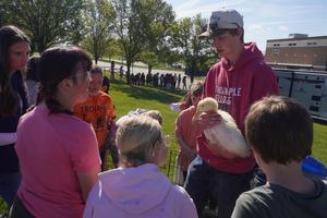 A student holds a duck while talking with elementary students.