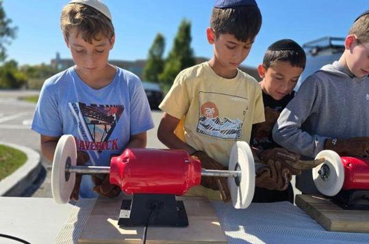 Boys working on woodworking projects with tools in an outdoor setting.