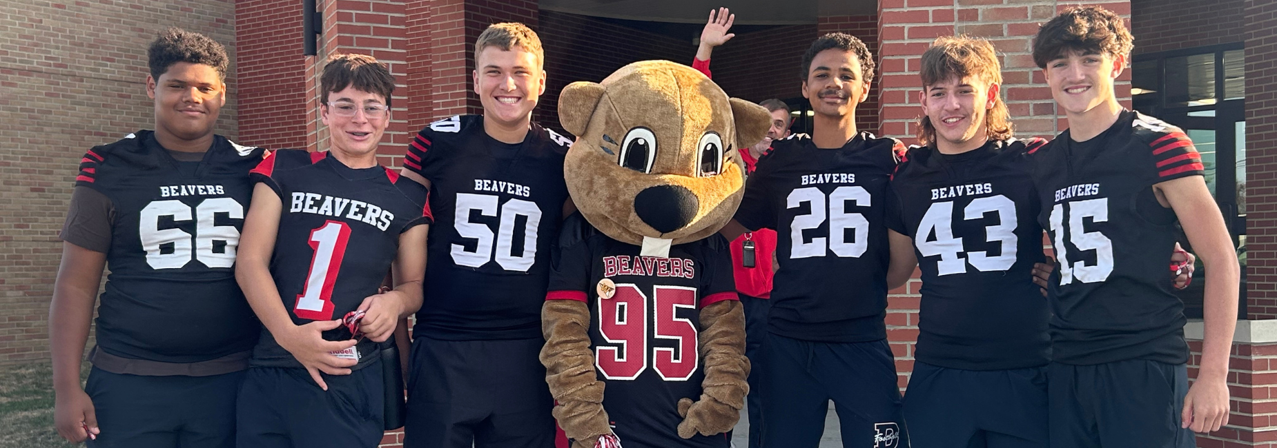 A group of students in football jerseys posing with a mascot outside.