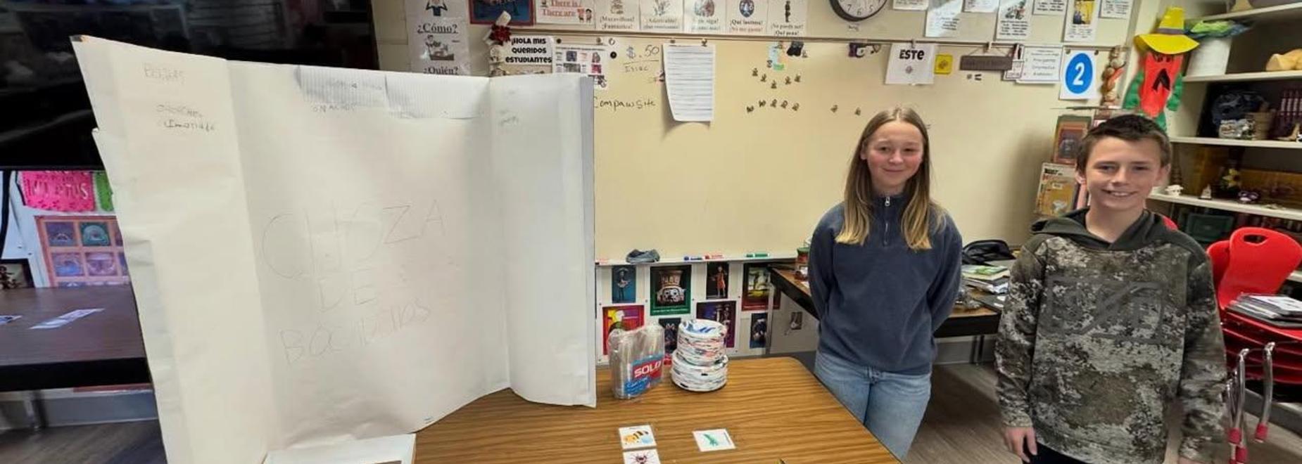 Two students standing beside a project display in a classroom with various educational materials.