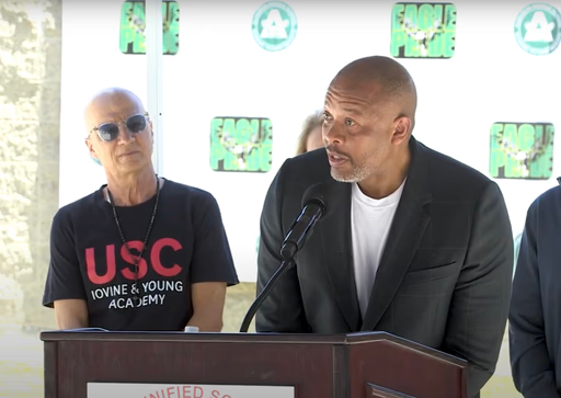 Dr. Dre speaks at a podium while Jimmy Iovine stands behind him