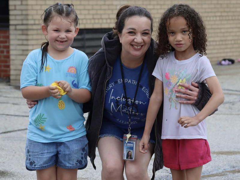 Two girls and a woman smiling outdoors, with one girl holding yellow Play-Doh.