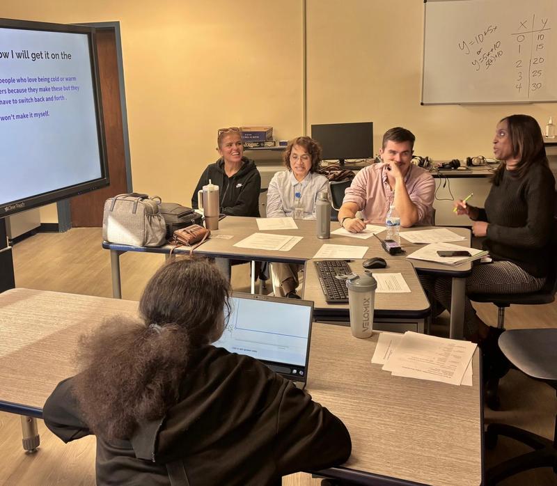A student presents a project on a laptop to four adults at a table.