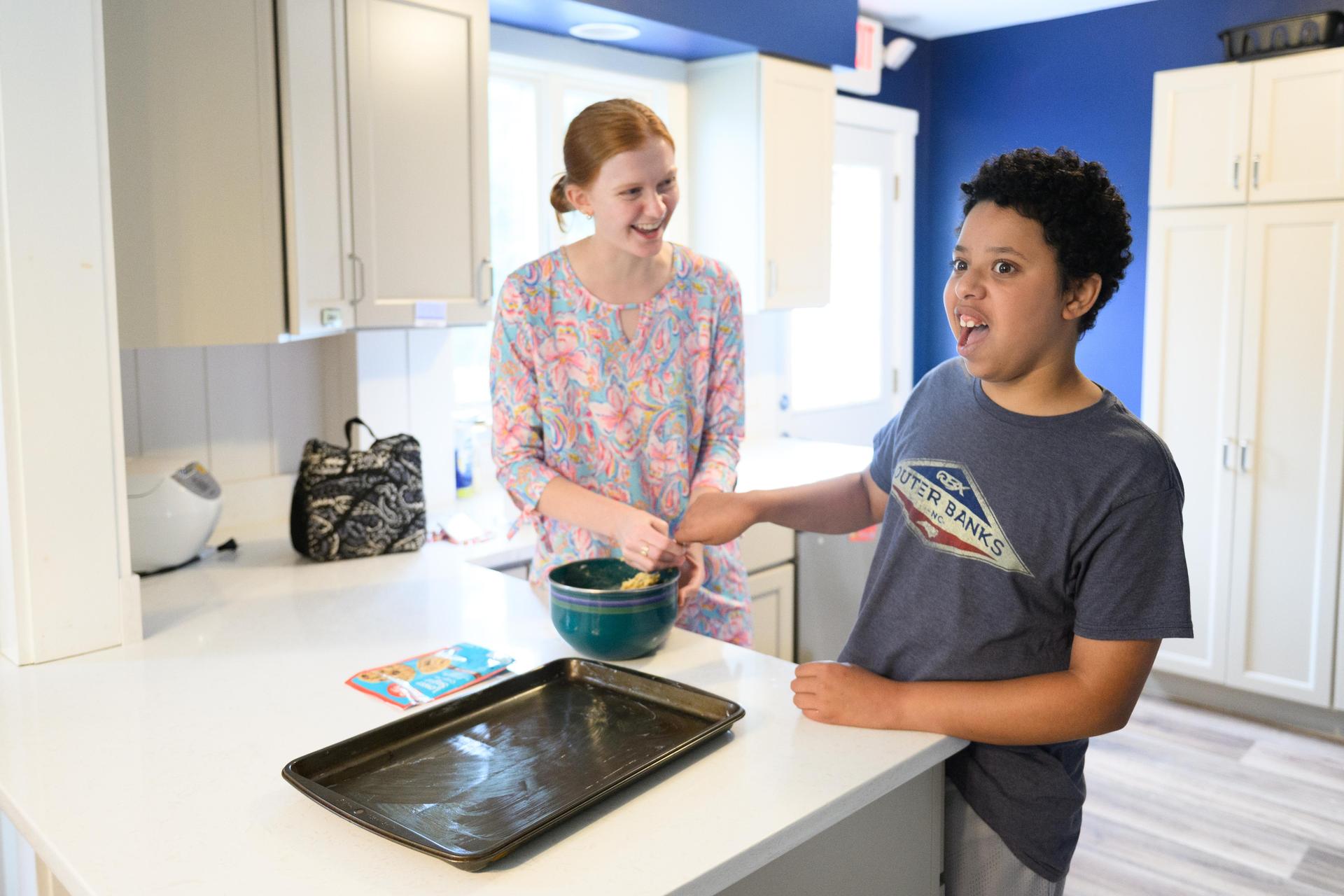 Teacher in pink and student in gray shirt mixing batter in kitchen.