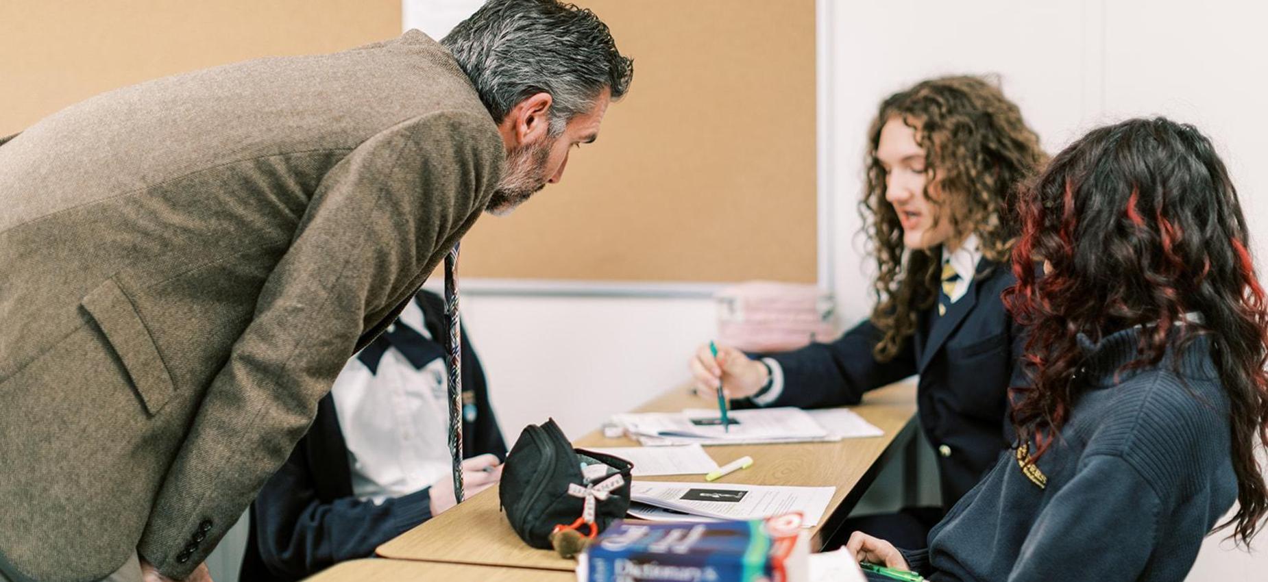 Teacher leans in to help high school students with their work