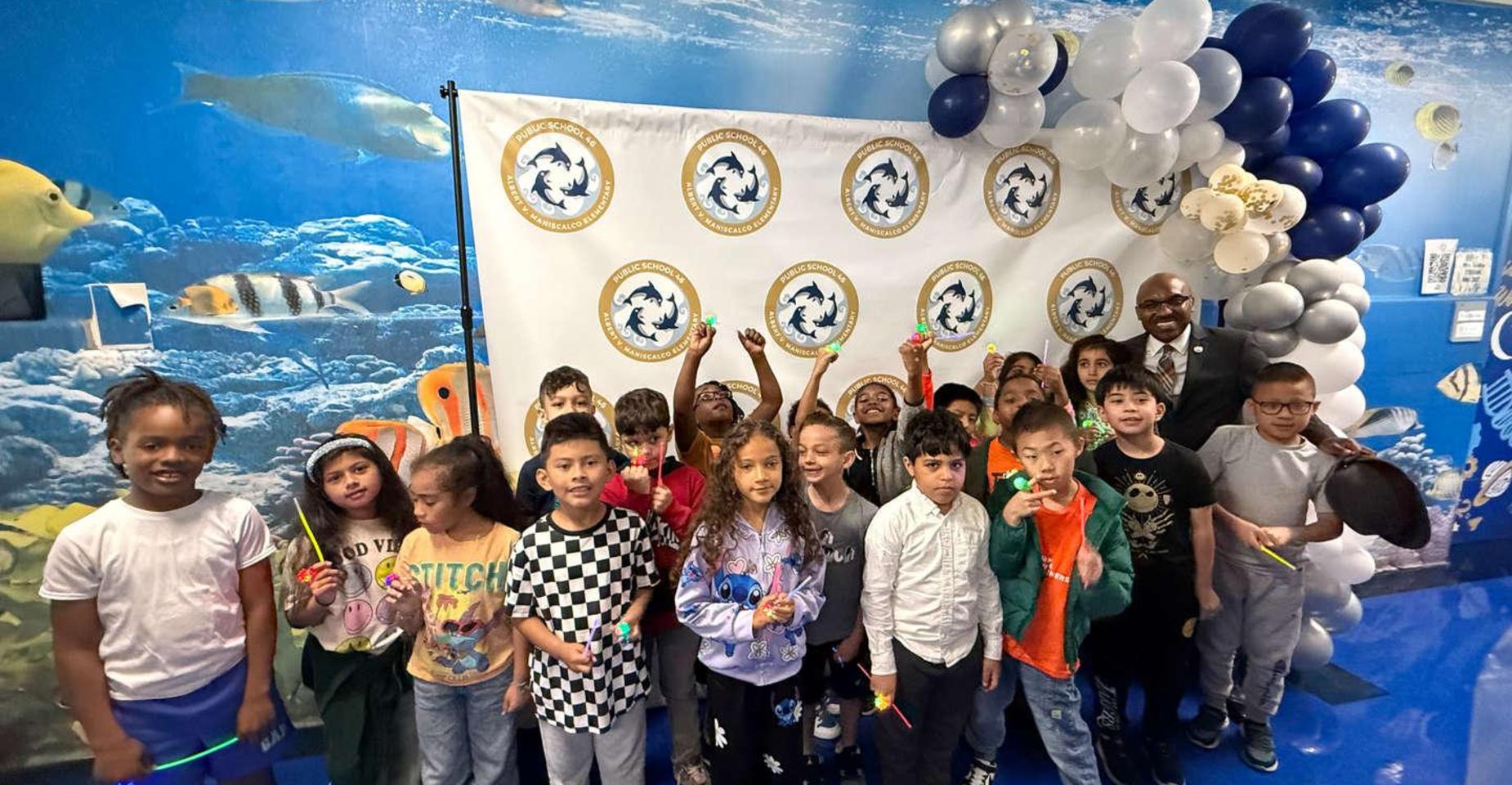 A group of children poses happily in front of a decorated backdrop.