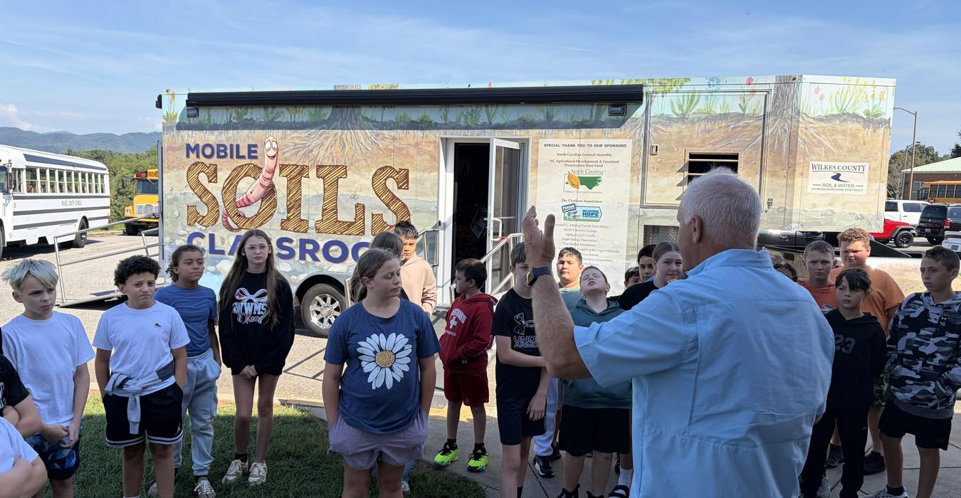 A group of students listening to an instructor near a mobile classroom.