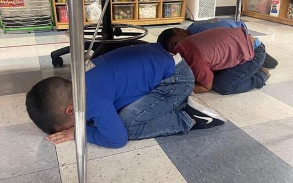 Children under the table practicing DROP COVER and HOLD.