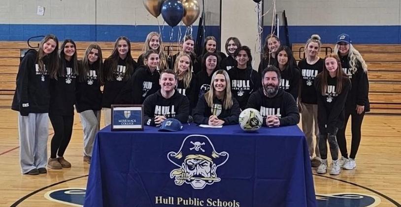 Team of female athletes seated around a table celebrating a sports signing event.