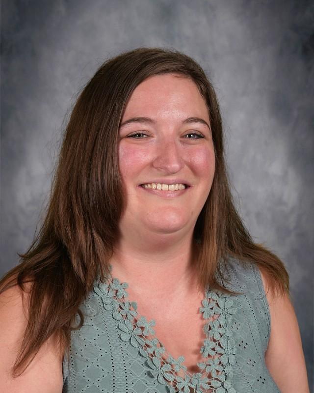 Smiling woman with long brown hair wearing a light pink sweater and a joyful expression.