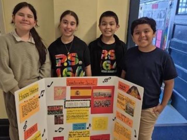 Four students pose with a project board featuring cultural information and decorations.