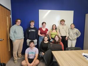 group of students that make up the trivia team leaning on blue wall