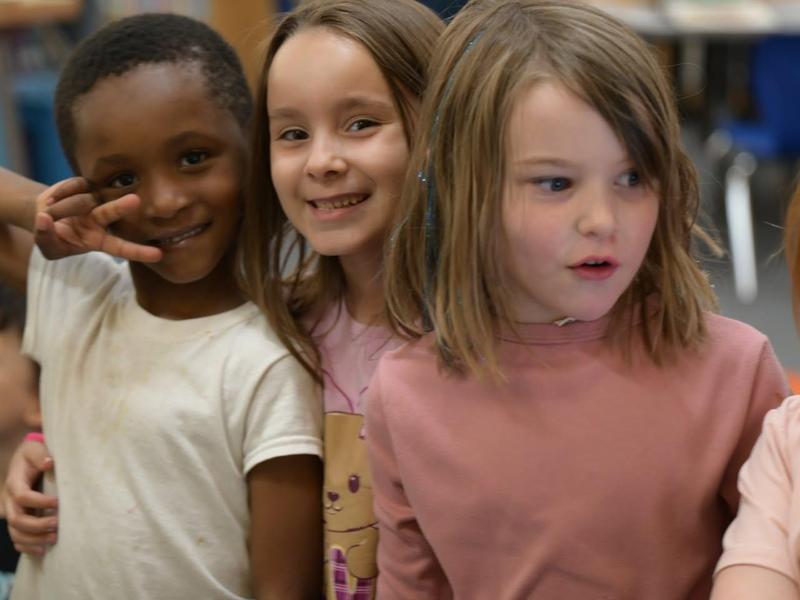 Two smiling children posing together with a third child in front.