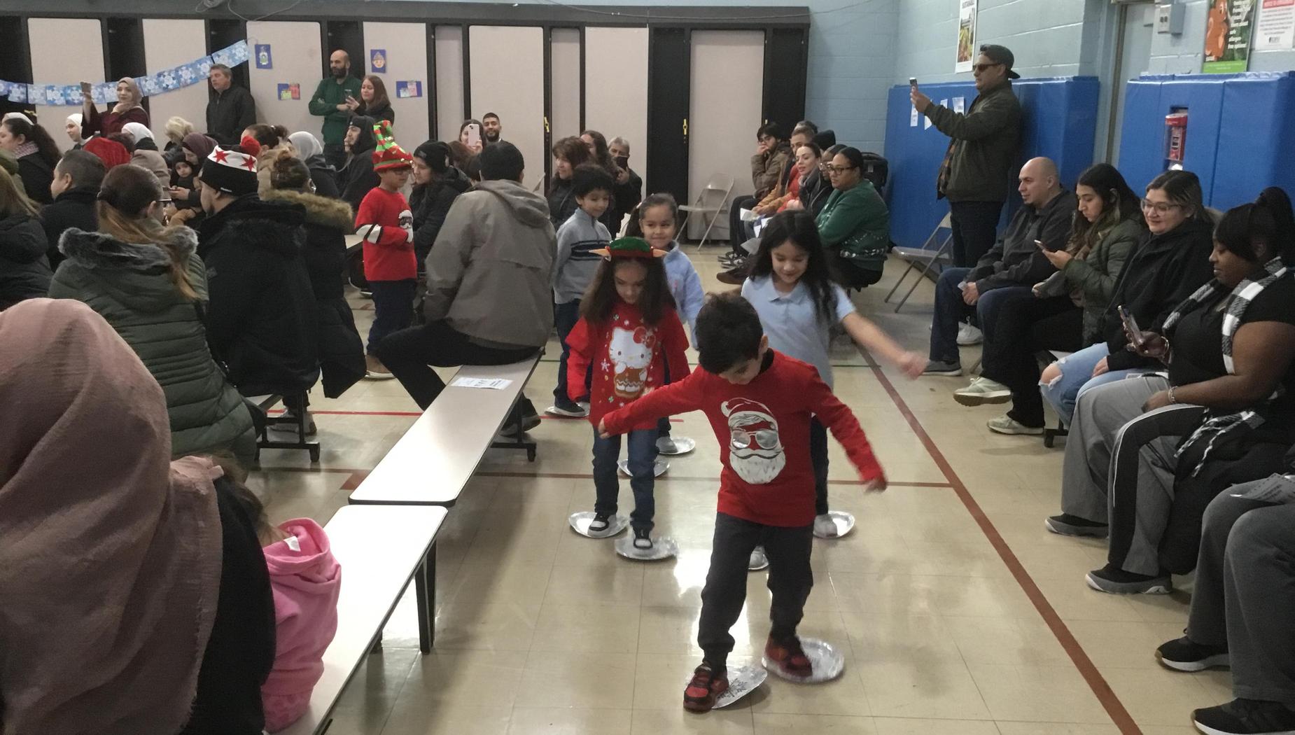 Children participating in a holiday event with an audience seated around them.