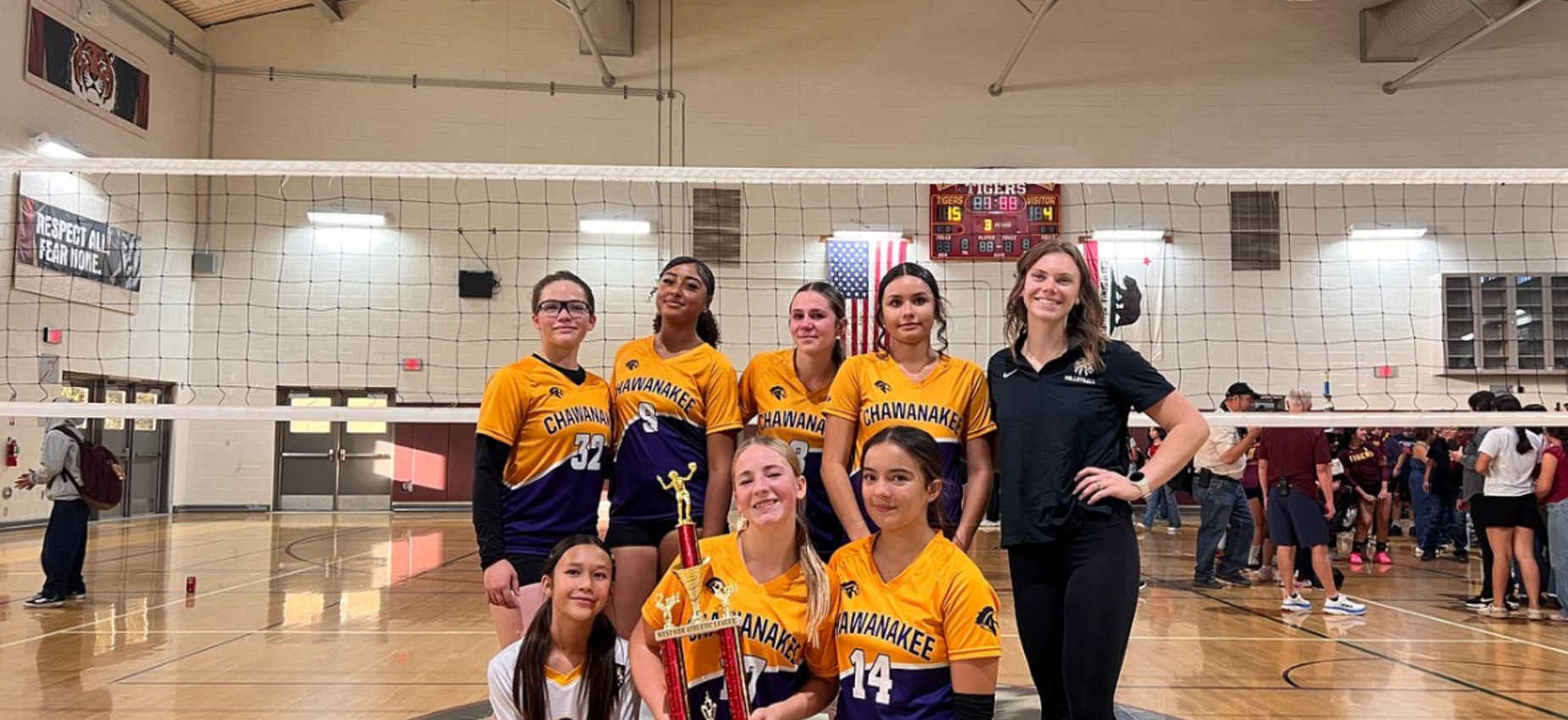 A volleyball team posing together with a trophy in a gymnasium.