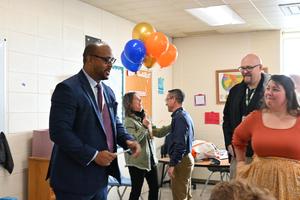 A group of six people celebrating with balloons in a classroom setting.